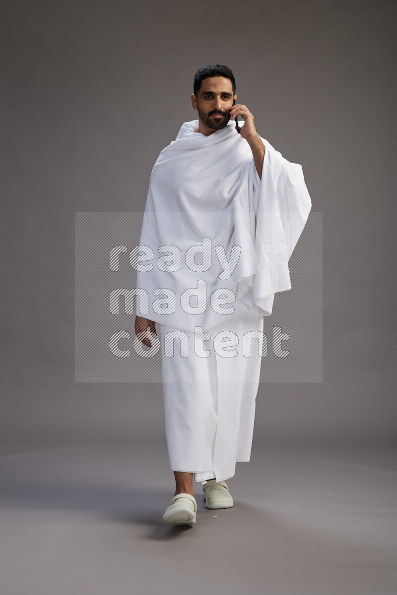 A man wearing Ehram Standing talking on phone on gray background