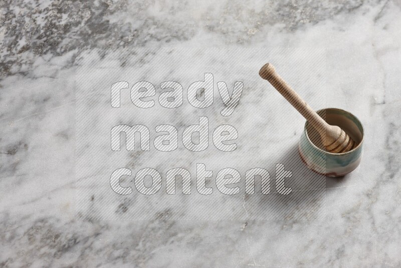 Multicolored pottery bowl with wooden honey dipper in it on grey marble background