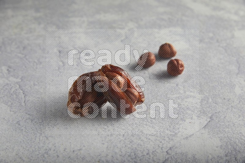 Two hazulnut stuffed dates with unroasted hazelnuts on light grey background
