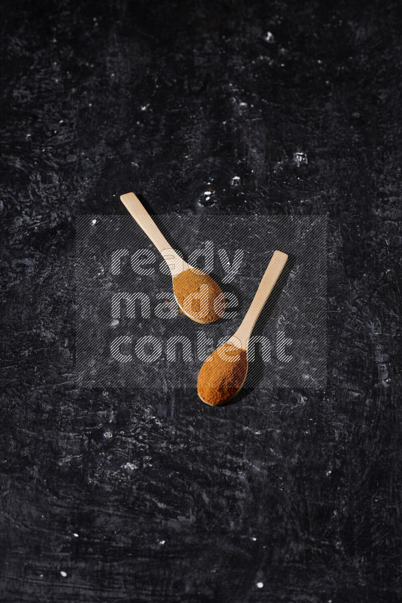 Two wooden spoons full of ground paprika powder on black background