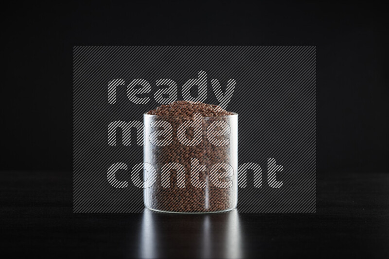 Brown lentils in a glass jar on black background