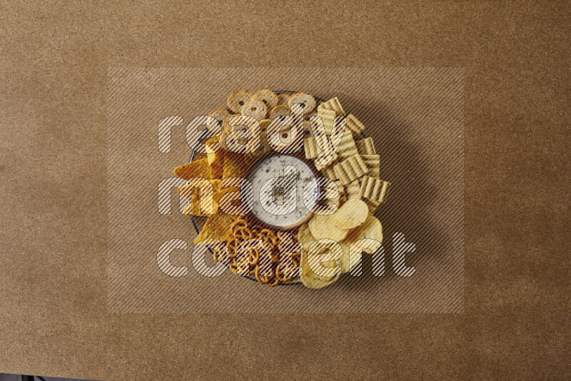 Assorted snacks on a pottery plate with a dipping on brown background