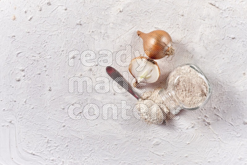 A glass jar full of onion powder flipped with some spilling powder on white background