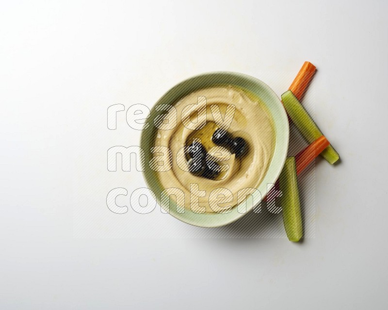 Hummus in a green plate garnished with black olives on a white background