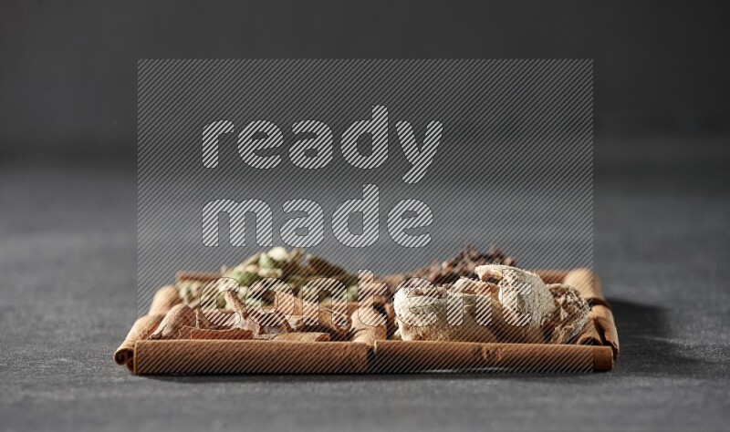 4 مربعات من عيدان القرفة ممتلئة بقطع القرفة وحبوب الهيل والقرنفل والزنجبيل المجفف على أرضية سوداء