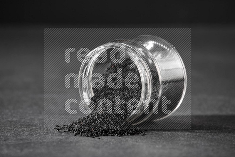 A flipped glass jar full of black seeds and the seeds spread out on a black flooring