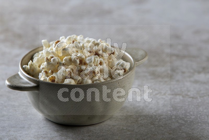 popcorn in a off-white handheld ceramic bowl on a grey textured countertop