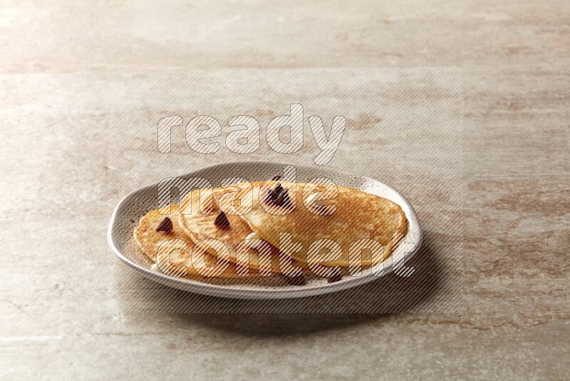Three stacked chocolate chips pancakes in an irregular plate on beige background