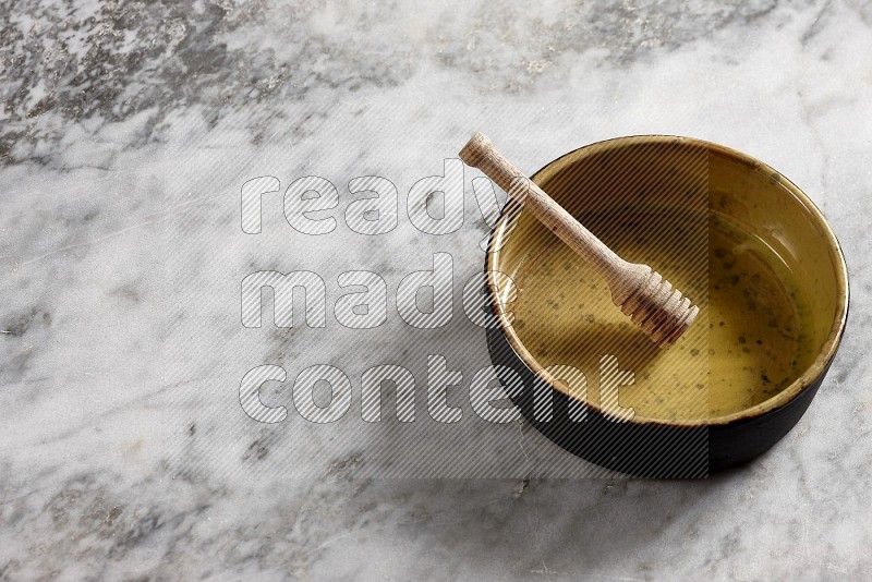 Multicolored Pottery Oven Plate with wooden honey handle in it, on grey marble flooring, 65 degree angle