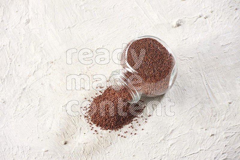 A glass spice jar full of garden cress and jar is flipped with fallen seeds on a textured white flooring in different angles