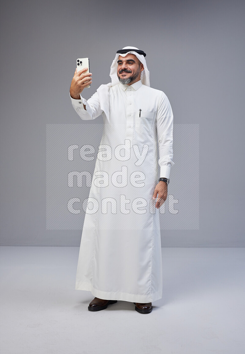 رجل سعودي يرتدي ثوب وشماغ ابيض يلتقط سلفي بجواله