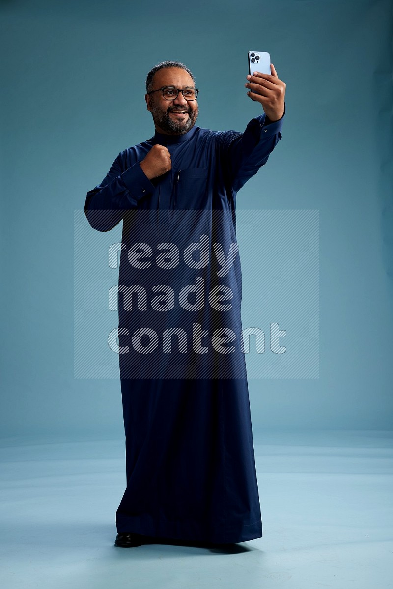 Saudi Man without shimag Standing taking selfie on blue background