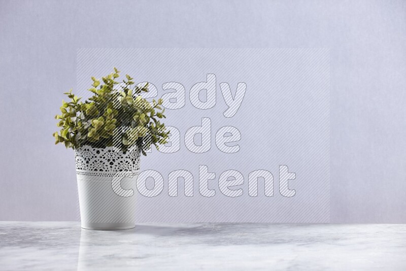 Green artificial plant in white decorative pot on grey marble background