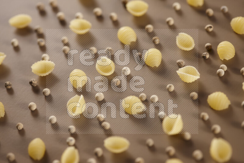 Raw pasta with different ingredients such as cherry tomatoes, garlic, onions, red chilis, black pepper, white pepper, bay laurel leaves, rosemary and cardamom on beige background