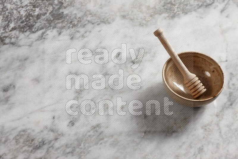 Beige pottery bowl with wooden honey dipper in it on grey marble background