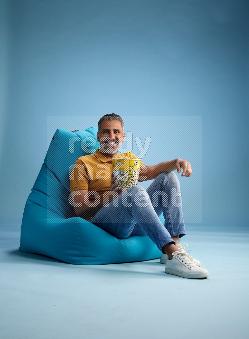 A man sitting on a blue beanbag and eating popcorn