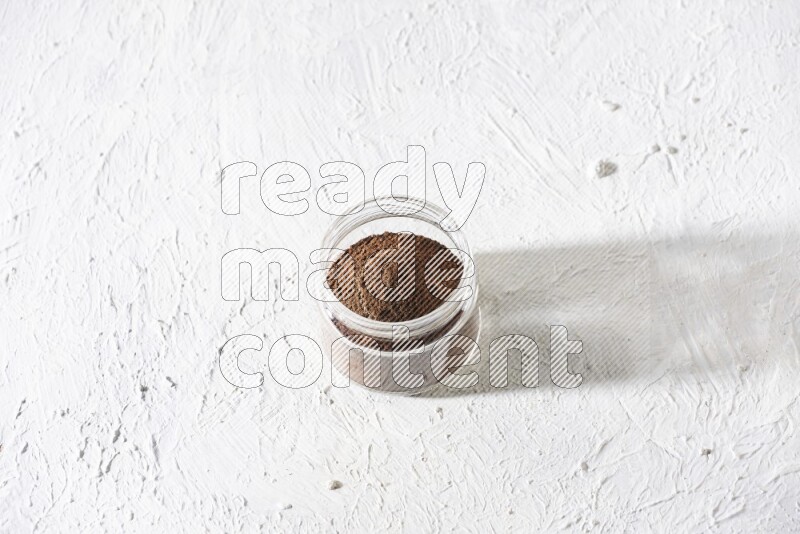 وعاء زجاجي ممتلئ ببودرة القرنفل على أرضية بيضاء