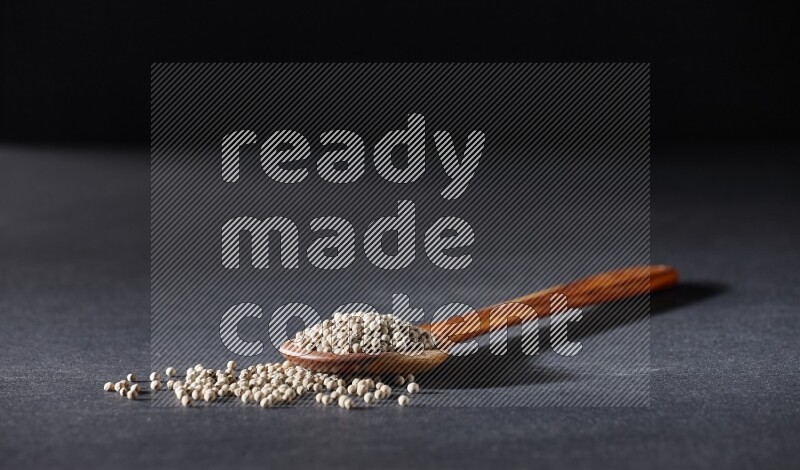 A wooden ladle full of white pepper beads on black flooring