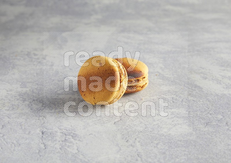 45º Shot of two Yellow Crème Brulée macarons on white  marble background