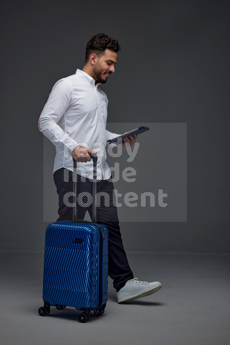 A man wearing smart casual with and pulling a carry-on luggage eye level on a gray background
