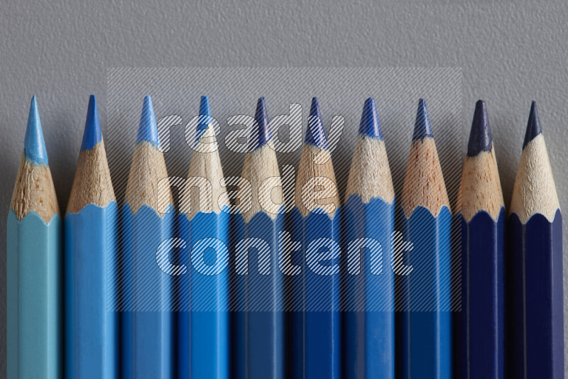 A collection of colored pencils arranged showcasing a gradient of blue hues on grey background