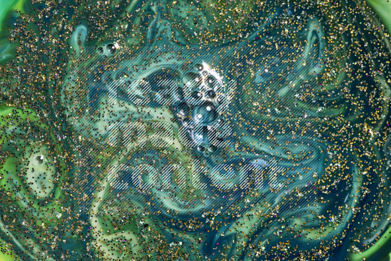 A close-up of sparkling gold glitter scattered on swirling blue and green background