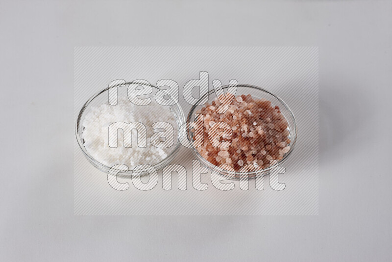 2 glass bowls one is filled with himalayan salt and the other with white salt on white background