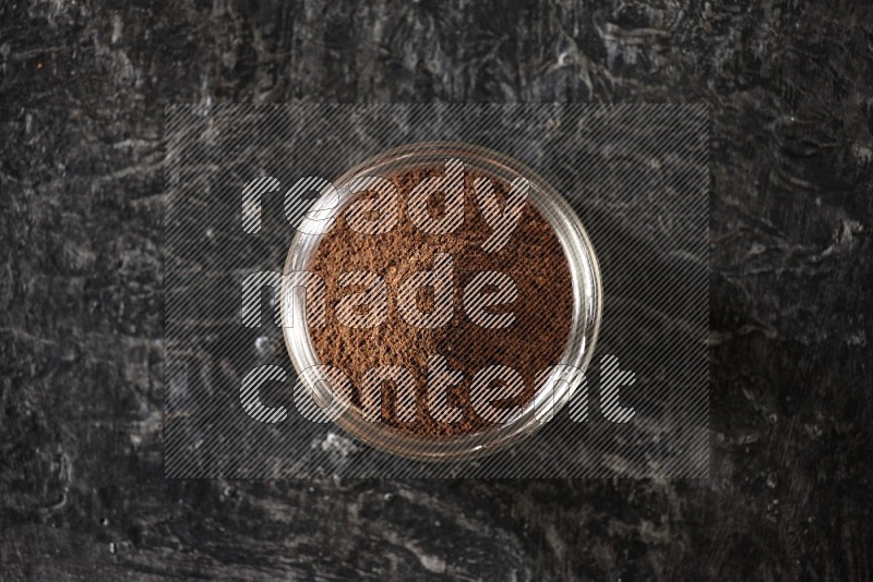 A glass jar full of cloves powder on a textured black flooring