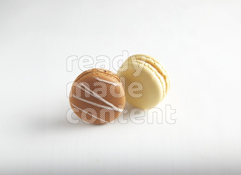 45º Shot of of two assorted Brown Irish Cream, and Yellow Vanilla macarons on white background