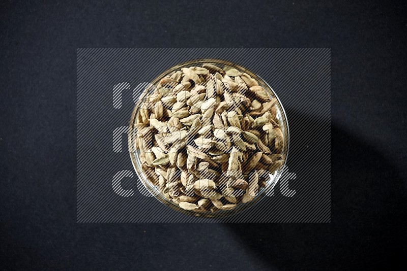 A glass bowl full of cardamom on black flooring