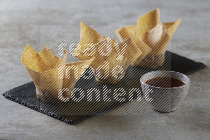 wonton cups with soy sauce ramkin on rectangle slate on grey textured counter top