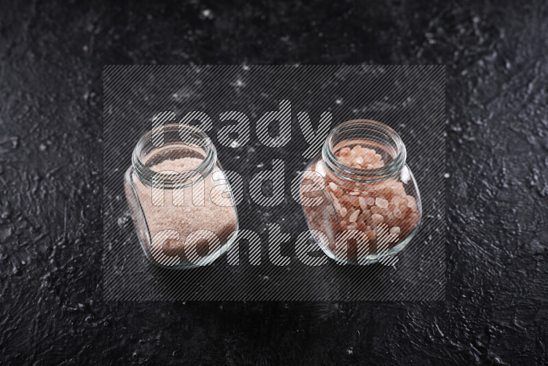 2 glass jars one is filled with fine himalayan salt and the other with coarse himalayan salt on black background