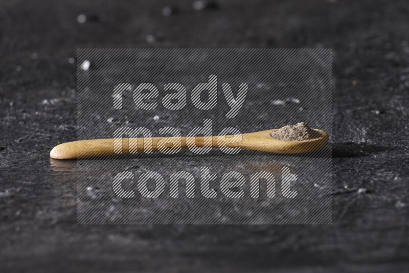 A wooden spoon full of black pepper powder on a textured black flooring