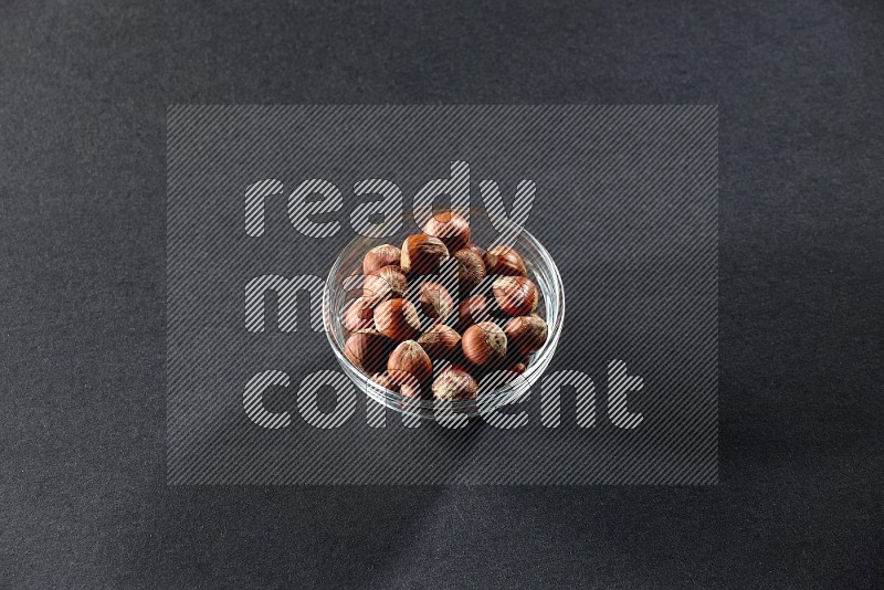 A glass bowl full of hazelnuts on a black background in different angles
