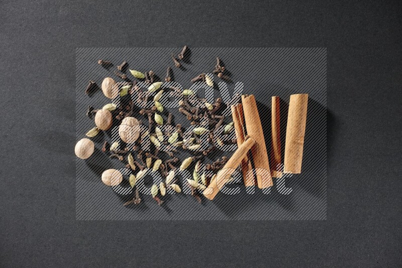 Cardamom, cloves, nutmeg and cinnamon sticks on black flooring
