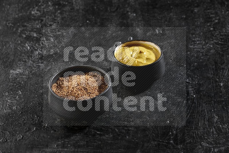 2 black pottery bowls full of mustard seeds and mustard paste on black flooring in different angles