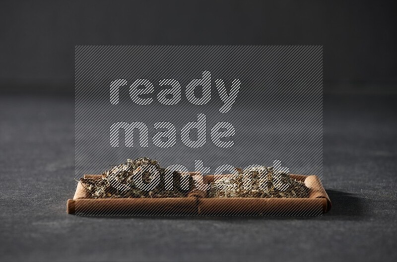 مربعان من أعواد القرفة ممتلئان بحبوب الكمون والريحان المجفف علي خلفية سوداء