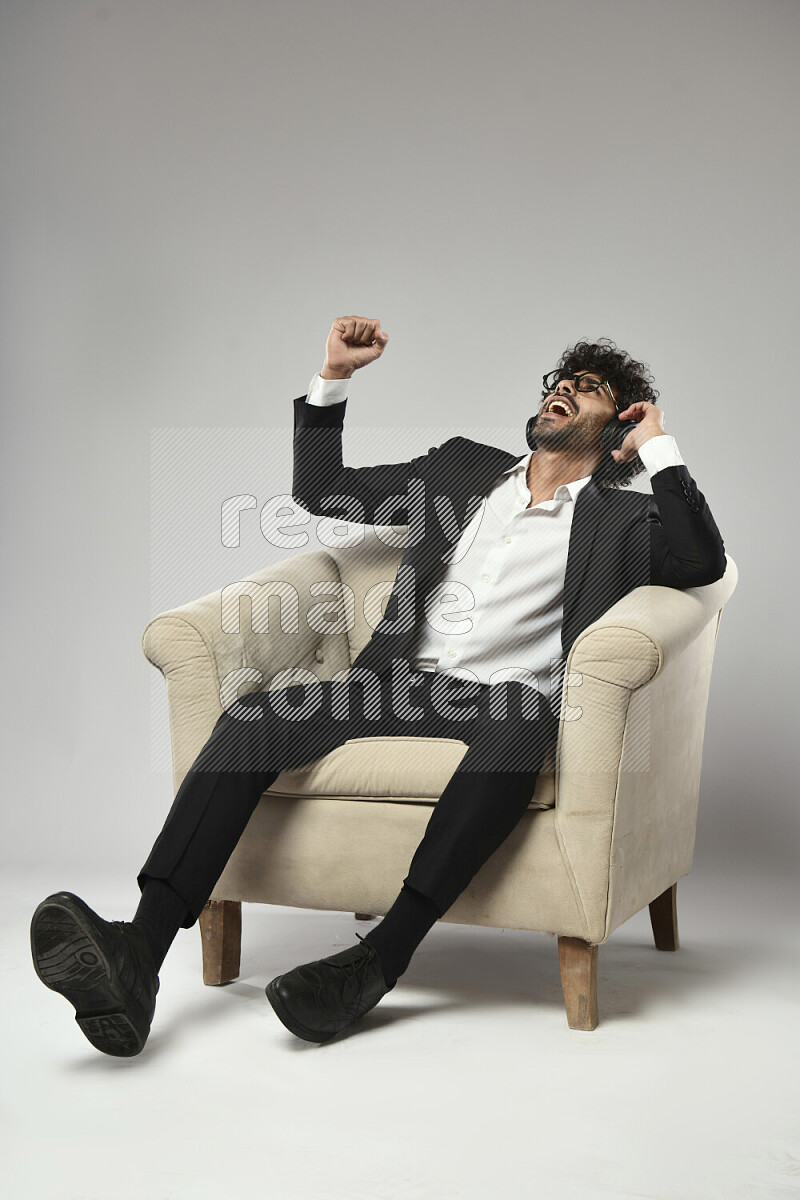 A man wearing formal sitting on a chair putting on headphones on white background