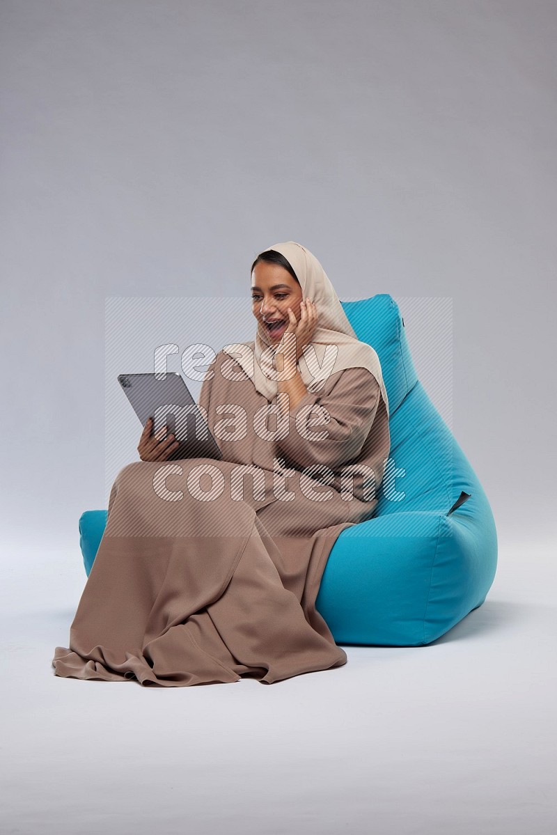 A Saudi woman sitting on a blue beanbag and working on tablet