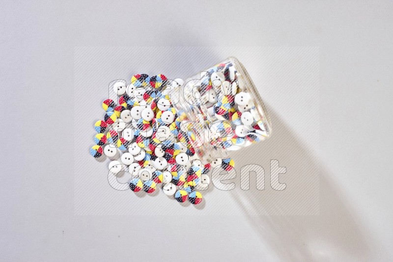 A glass jar full of colored buttons on grey background