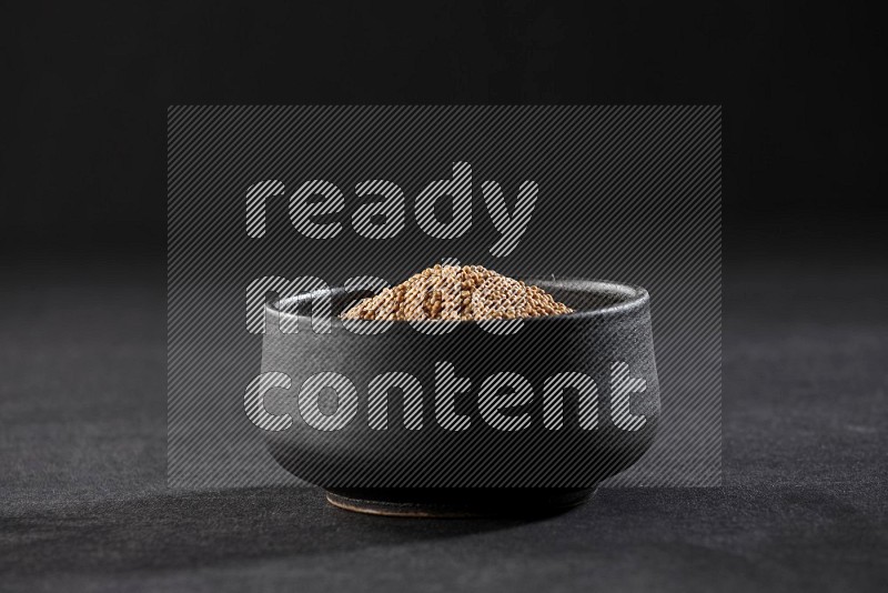 A black pottery bowl full of mustard seeds on black flooring