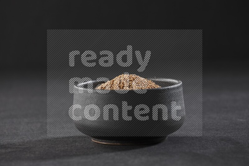 A black pottery bowl full of mustard seeds on black flooring