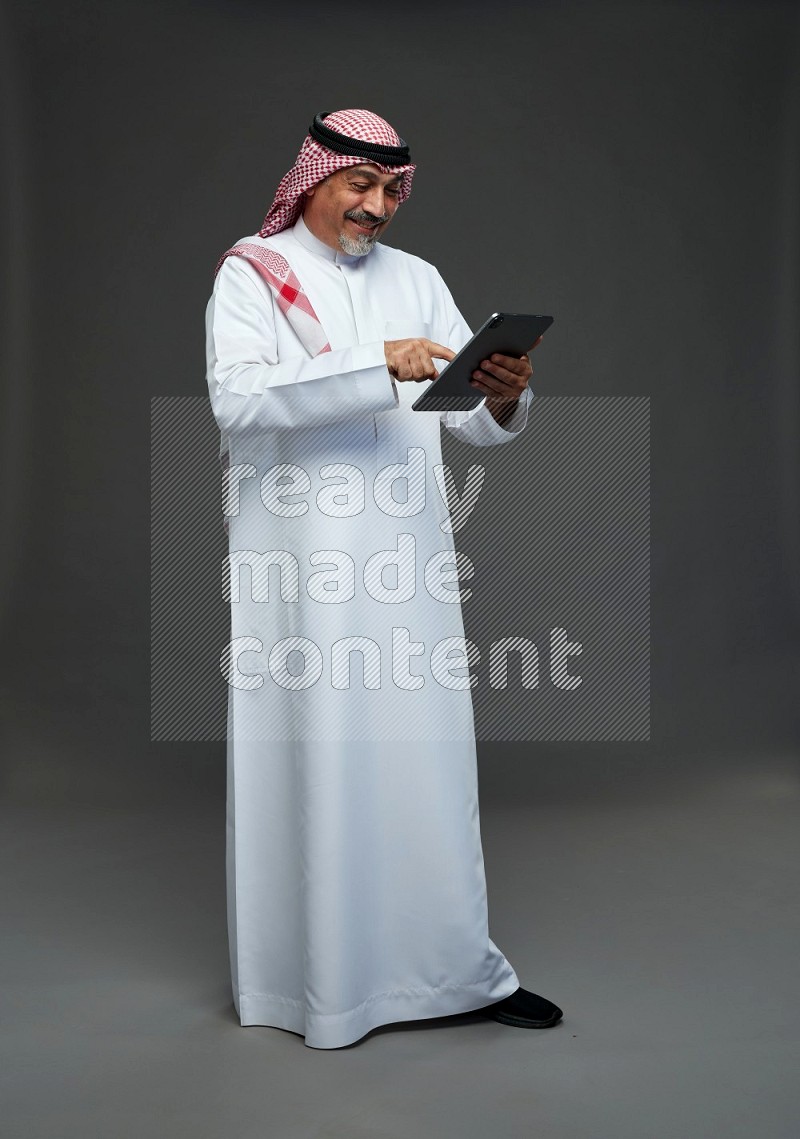 Saudi man with shomag Standing working on tablet on gray background