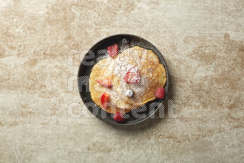 Three stacked mixed berries pancakes in a black plate on beige background