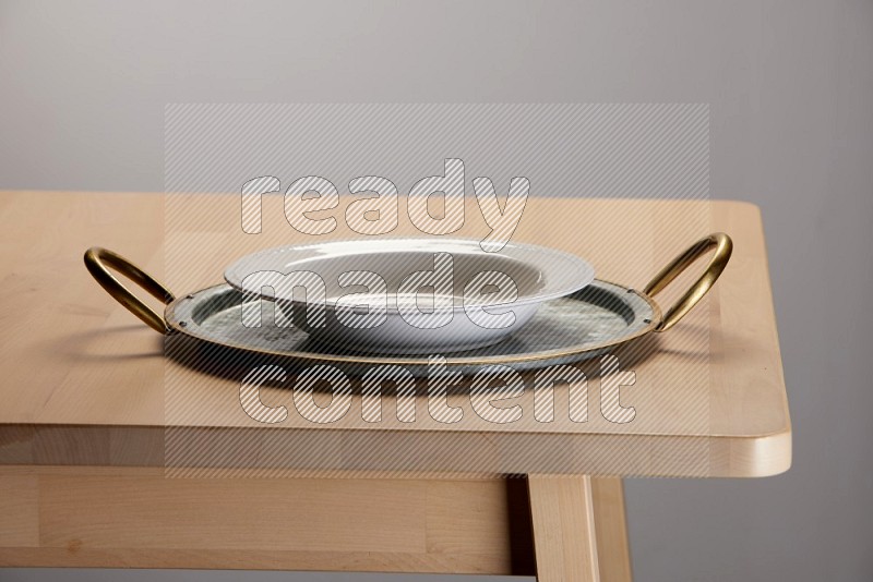 white plate placed on a rounded stainless steel tray with golden handels on the edge of wooden table