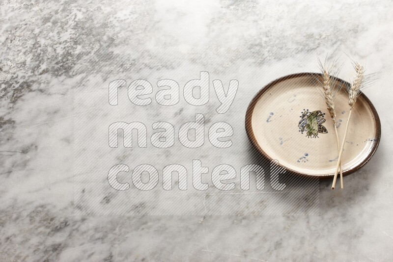 Wheat stalks on decorative pottery plate on grey marble background