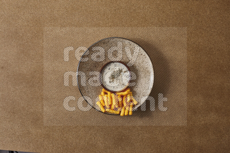 Assorted snacks on a pottery plate with a dipping on brown background