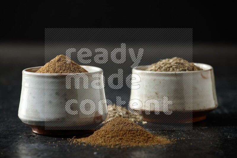 وعاءين بيج، أحدهما ممتلئ ببودرة الكمون والآخر ممتلئ بحبوب الكمون، على خلفية سوداء