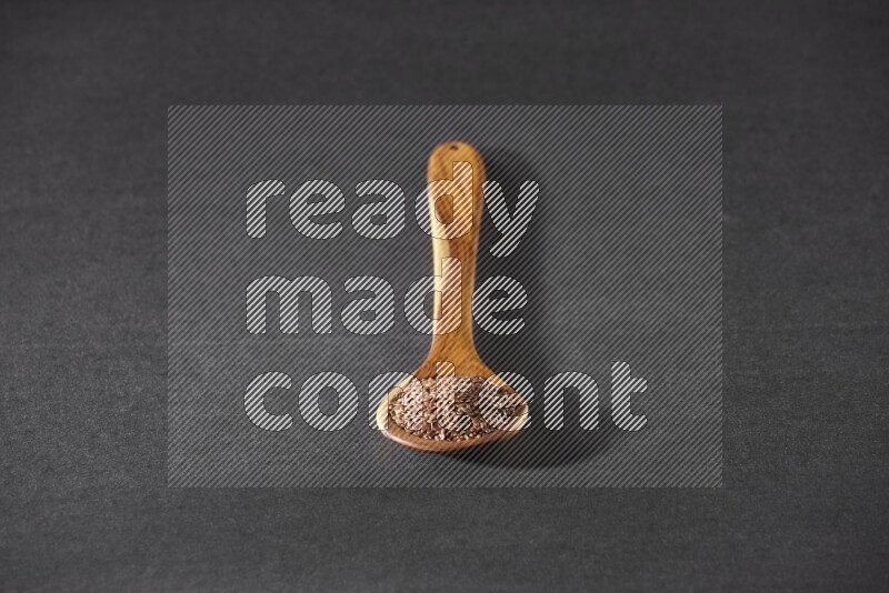 ملعقة خشبية كبيرة ممتلئة بحبوب بذر الكتان علي خلفية سوداء