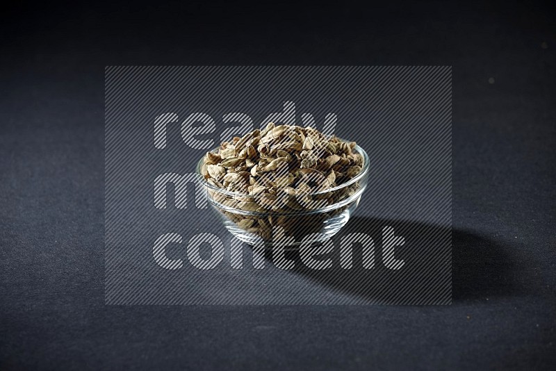 A glass bowl full of cardamom on black flooring